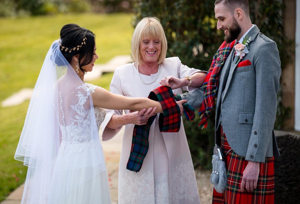 A picture of a bride and groom on their wedding day with their celebrant performing the hand fasting gesture