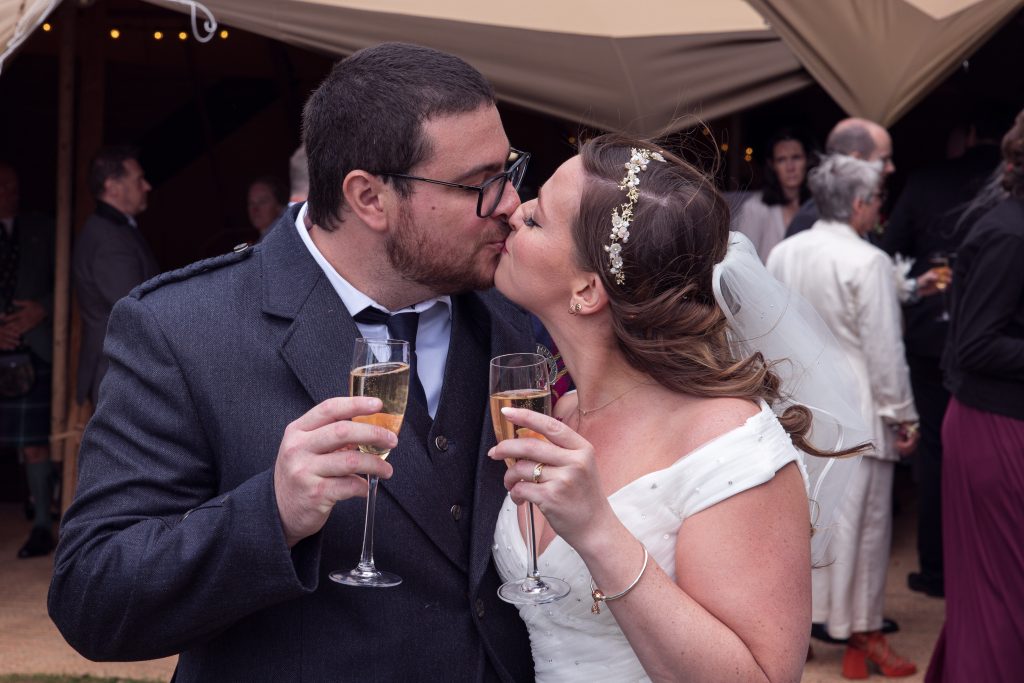 bride and groom kissing, glass of champagne, tipi, wedding