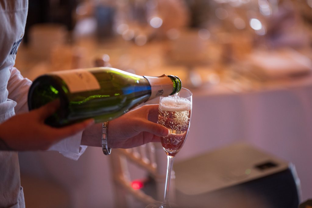A person serving champagne in a flute glass during a wedding drinks reception.