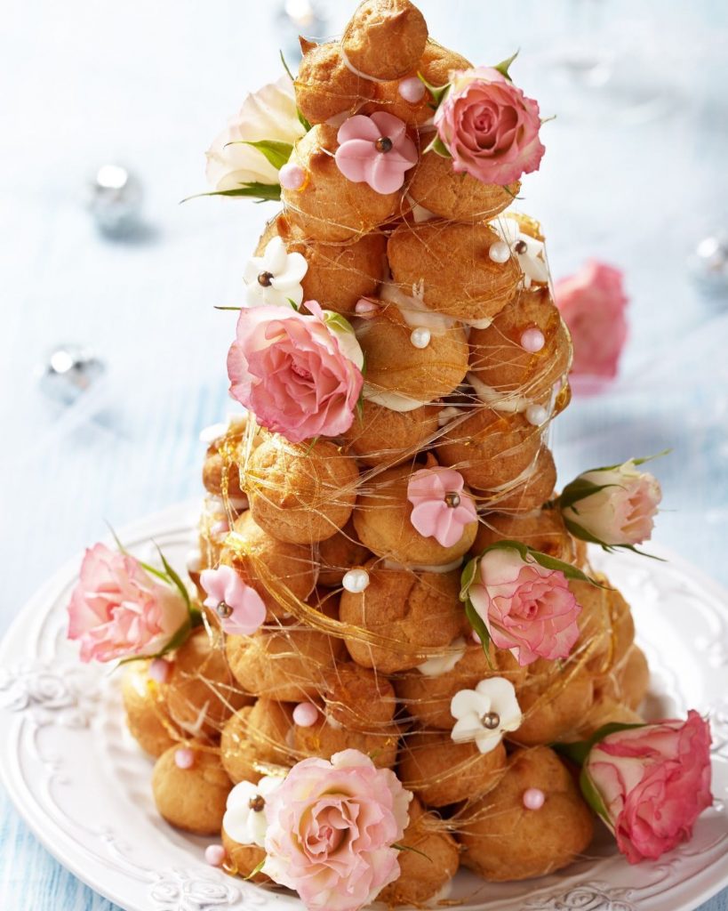 A tower of mini choux also called croquembouche, a traditional wedding cake in France, with pink and white sugar flowers.