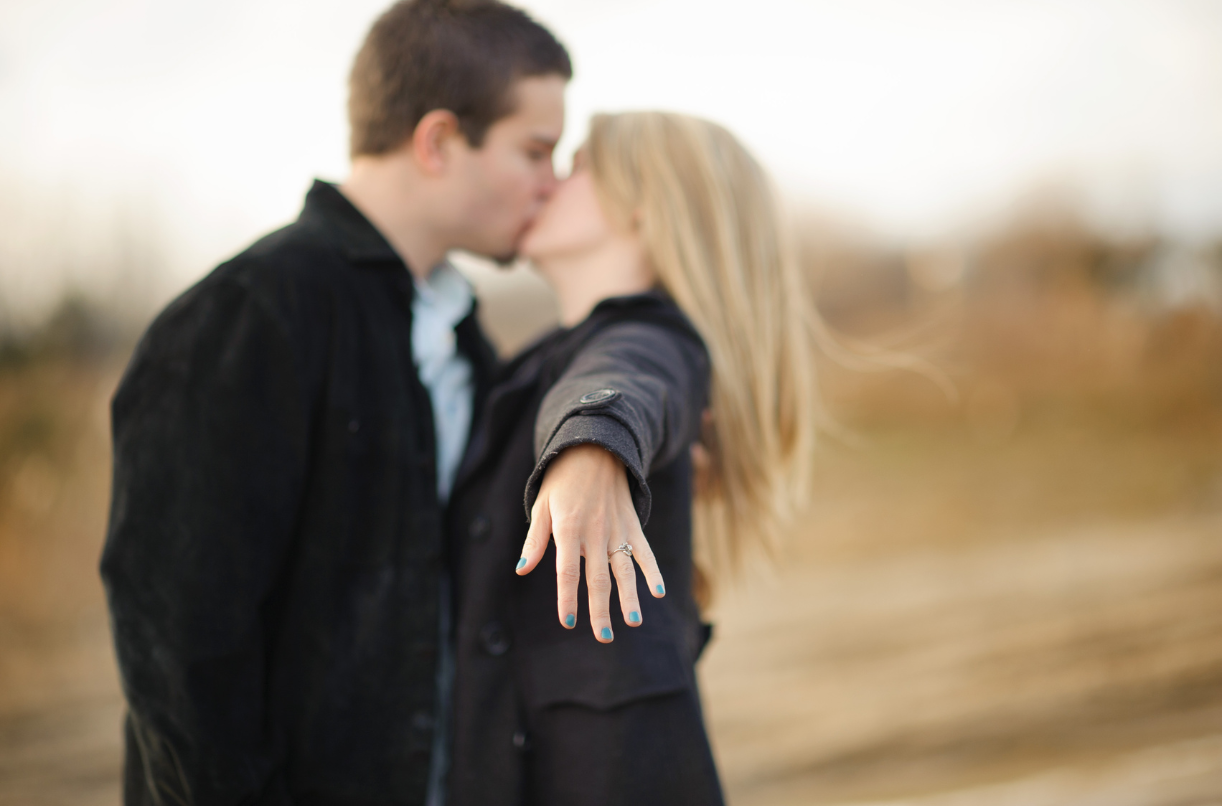A couple kissing with the woman showing her engagement ring